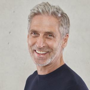 Man with grey hair smiles while facing camera.