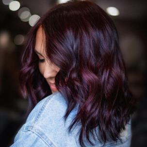 Model with black plum hair color looks over her shoulder. They wear a light denim jacket