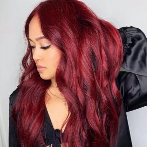 Headshot of a person with long wavy ruby red hair wearing a black satin jacket