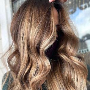 Model with long, wavy hair and caramel brown balayage.