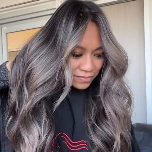 Model with long black hair and silver balayage, styled in loose waves.
