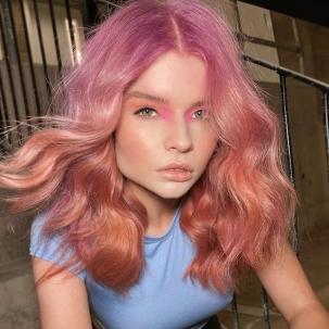 Model with wavy, pink and peach ombre hair faces the camera.