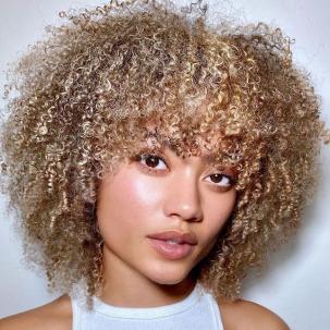 Model faces the camera with short, curly, sandy blonde hair and bangs.