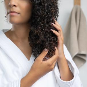 Model smooths ULTIMATE SMOOTH Miracle Oil Serum through their dark, curly hair.