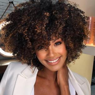 Woman smiles at the camera with curly, iced caramel espresso hair color.