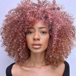 Model with long, curly hair in a radiant rose gold shade.