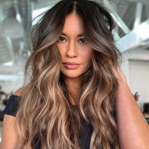 Model with long, wavy, brunette hair and a caramel blonde balayage faces camera.