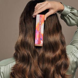 Back of model’s head with long, wavy, brunette hair. They are holding a box of Color Touch demi-permanent hair colour.