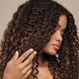 Model sweeps long, dark, curly hair away from her face.