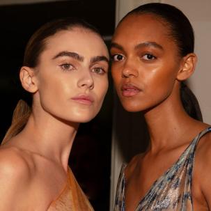 Two models with sleek, low ponytails posing backstage at Victoria Beckham’s SS25 show.