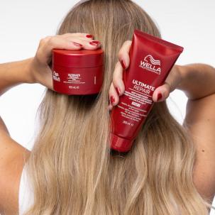 Hinterkopf eines Models mit langem, glattem, goldblondem Haar. Sie hält die ULTIMATE REPAIR Maske und den Conditioner hoch.