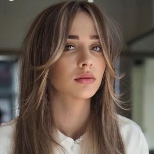 Model with long brown hair and highlighted bangs faces the camera.