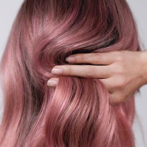 Close-up of a person's hand with pale pink painted nails running fingers through their pink hair