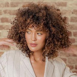 Model with chocolate brown, curly hair gazes off to the side.