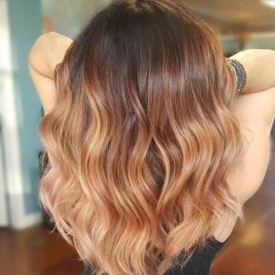 Back of woman's head with dark roots and caramel blonde hair styled with loose waves