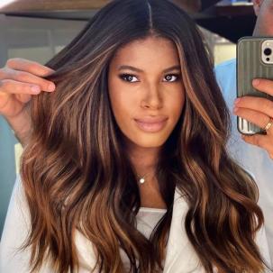 Model with long, loosely waved, dark brown hair and copper highlights sits in the salon chair.