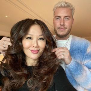 Hairdresser finishes styling a model’s long, dark brown, loosely curled hair.