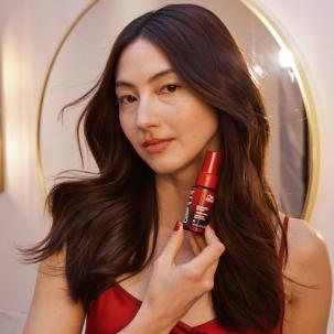 Model with long, dark hair styled in loose waves holds up ULTIMATE REPAIR Night Serum.