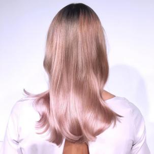 Back of womans head with long straight pastel pink hair and dark roots