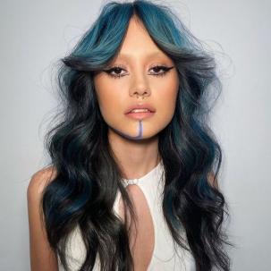 Model with dark hair and blue face-framing highlights faces the camera.