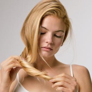 Model looks at the ends of their blonde hair.