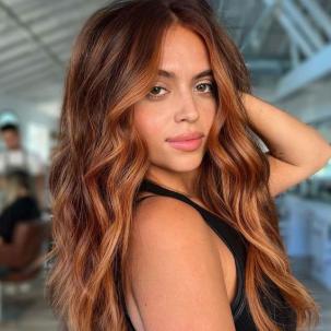 Model with long, wavy, copper brown hair smiles at the camera.