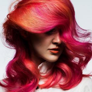 Woman with bright orange red pink hair, styled with loose waves