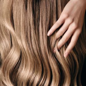 Close-up of fingers running through long, wavy, dark blonde hair. 