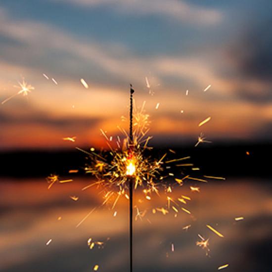 Photo of a sparkler in the foreground and the sunset in the background.