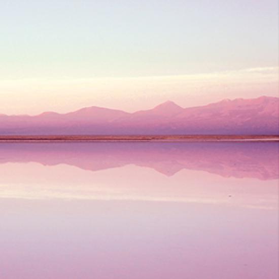 Pink colored mountains and grey sky reflected in the water below