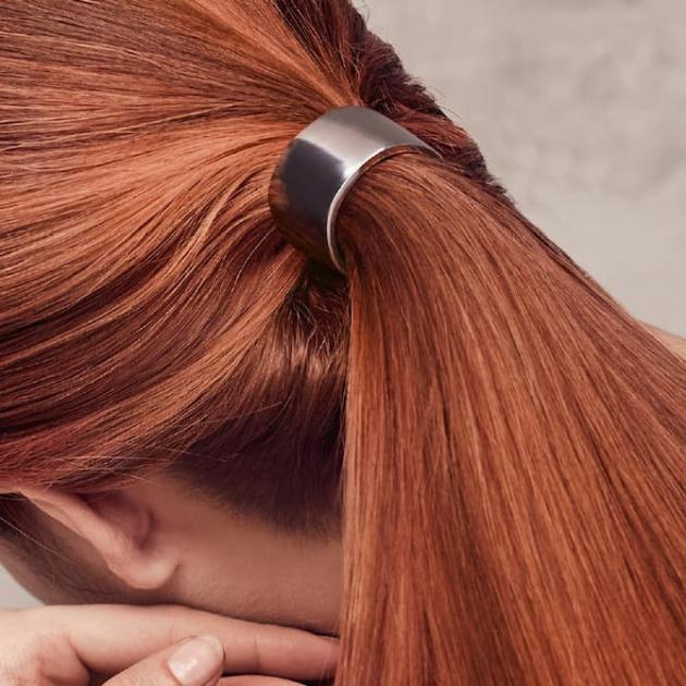 Photo of the back of a woman’s head, with glossy red hair tied in a low ponytail.