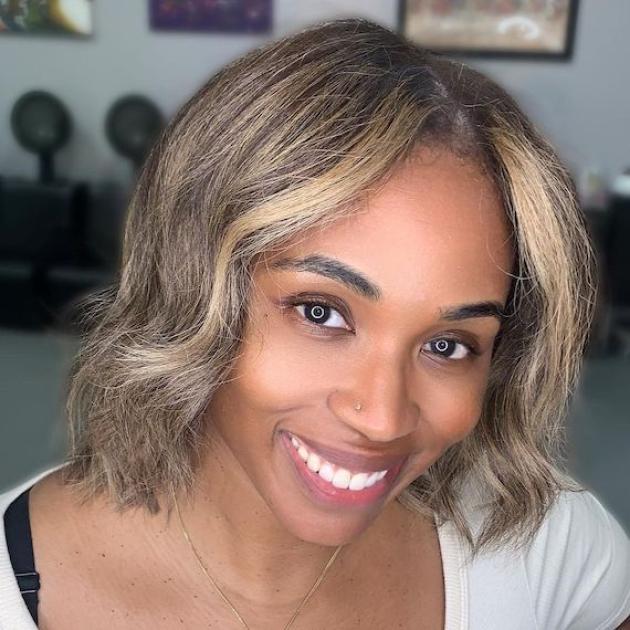 Model with short, dark, bob haircut and blonde highlights smiles at the camera.