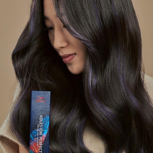 model with long, black hair looks to the side whilst holding a box of Koleston Perfect by Wella Professionals