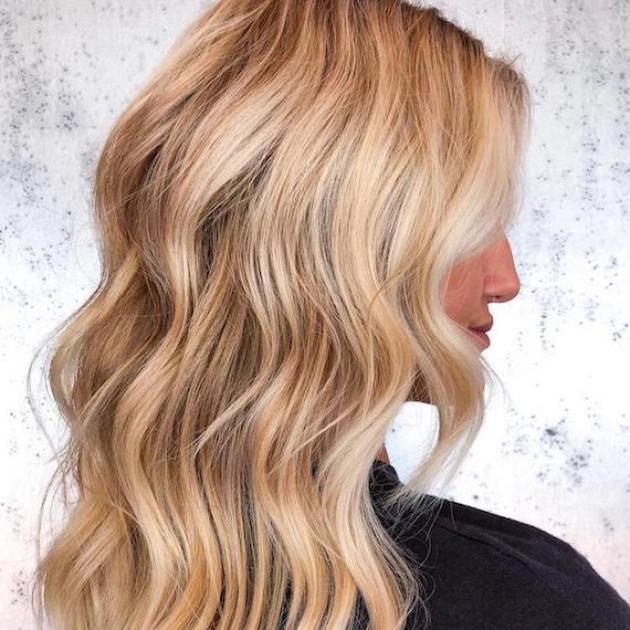 Side profile of woman with long, wavy hair and honey blonde balayage, created using Wella Professionals.