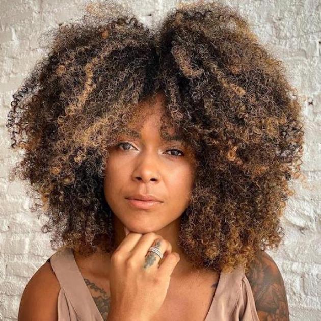 Woman faces camera with curly brown hair and blonde balayage, created using Wella Professionals.