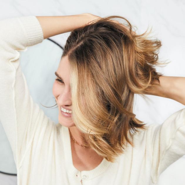 Woman smiles as she tousles her glossy brown hair.