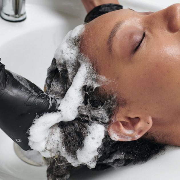 Close-up of model having their long, dark hair washed in a salon sink.