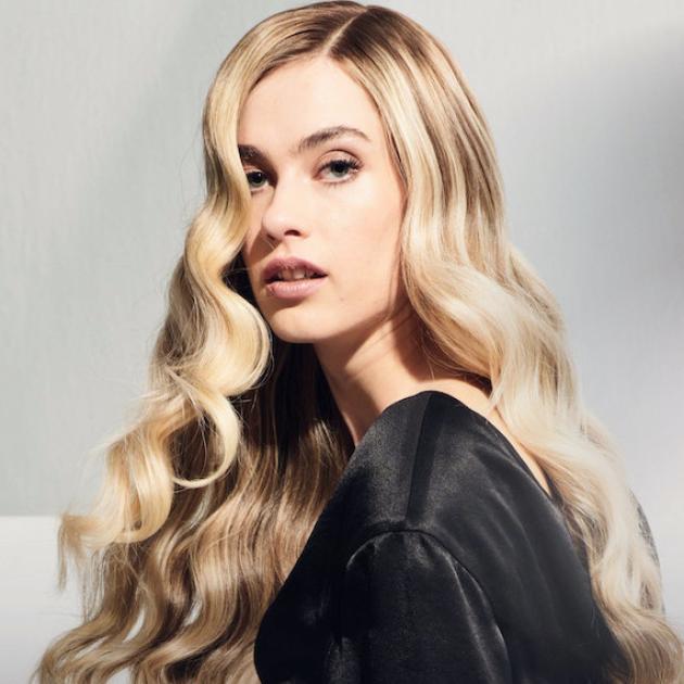 Model with long, wavy blonde hair looks over her shoulder.