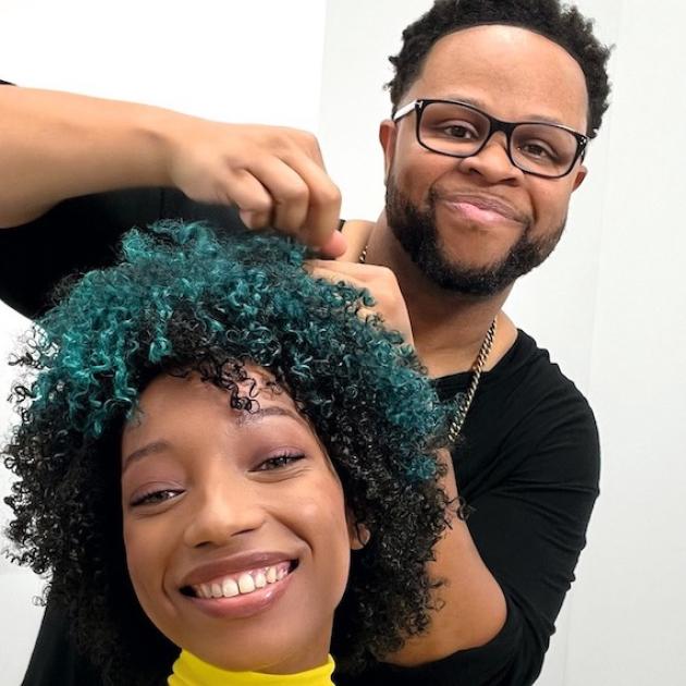 Hairdresser styles model hair as they both smile into the camera.