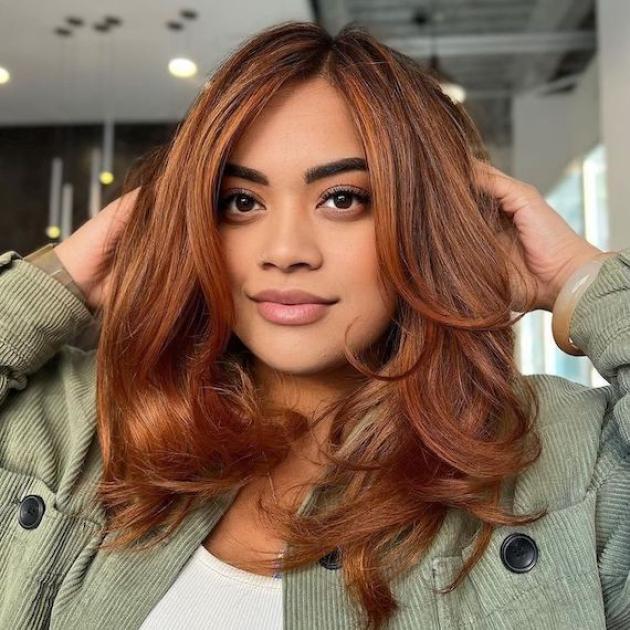 Model with copper red hair styles in loose waves smiles at the camera.