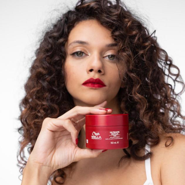 Model with brown, curly hair holds up the ULTIMATE REPAIR Mask.