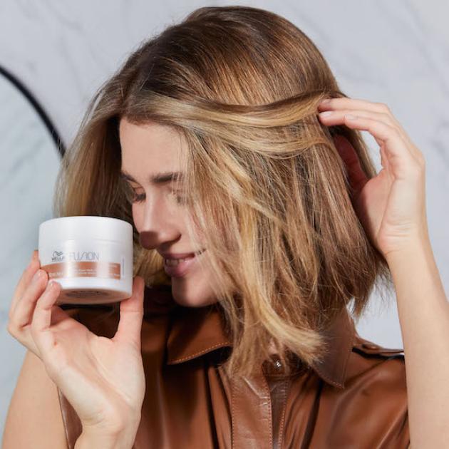 Model sweeps hair back while holding a jar of Wella’s Fusion Intense Repair Mask.