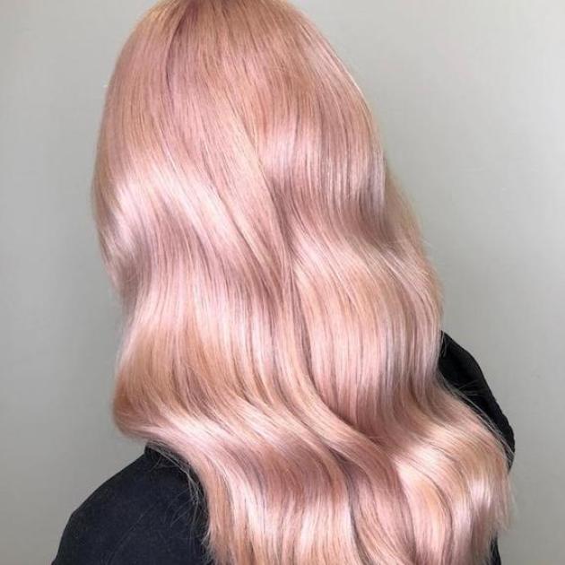 Hinterkopf einer Frau mit langem, gewelltem, pastellrosé-goldenem Haar, kreiert mit Wella Professionals.