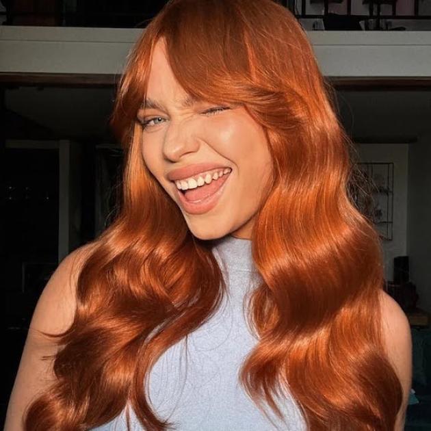 Model with long, copper red, wavy hair and grown-out bangs.