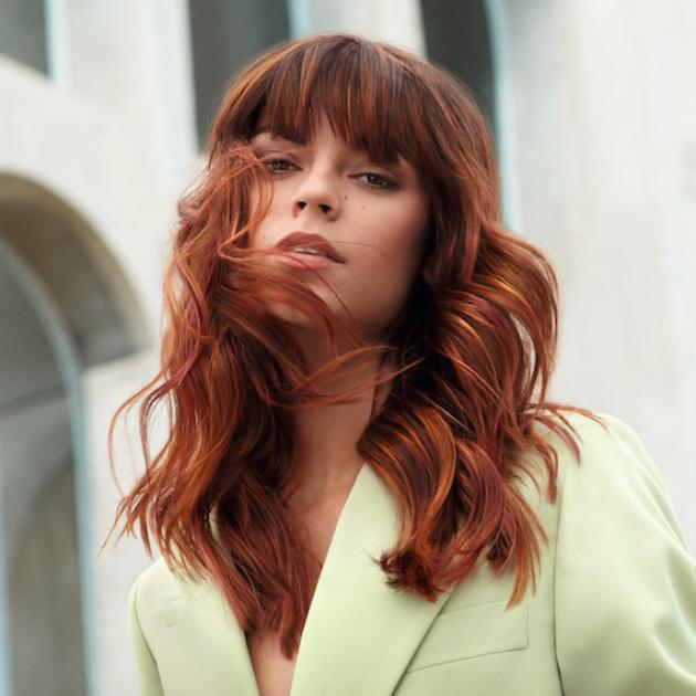 Model with wavy copper hair and fringe looks into the camera.