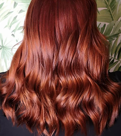 Back of woman’s head with long, loosely curled, glossy auburn hair, created using Wella Professionals.