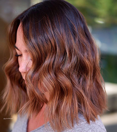 Side profile of woman with short, wavy, brown balayage bob, created using Wella Professionals.