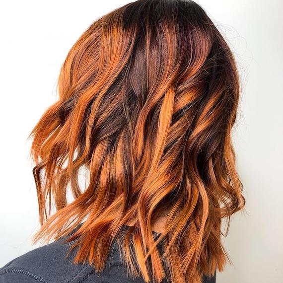 Model with wavy, pumpkin spice hair and balayage, created using Wella Professionals. 