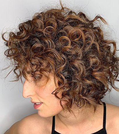 Side profile of a person with short chocolate brown hair styled in tight curls