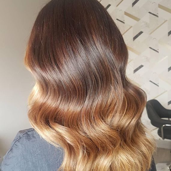 A person with long brown hair and a honey blonde ombre has their back facing the camera. 
